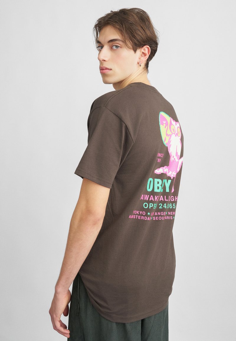 Brun bomulds t-shirt, rund hals, korte ærmer, med farverigt grafik på ryggen med tekst i pink og turkis. Afslappet pasform.