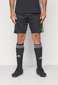 Sorte idrettsshorts med grønne striper, kombinert med sorte sokker med hvite striper og hvit logo, samt sorte fotballsko.
