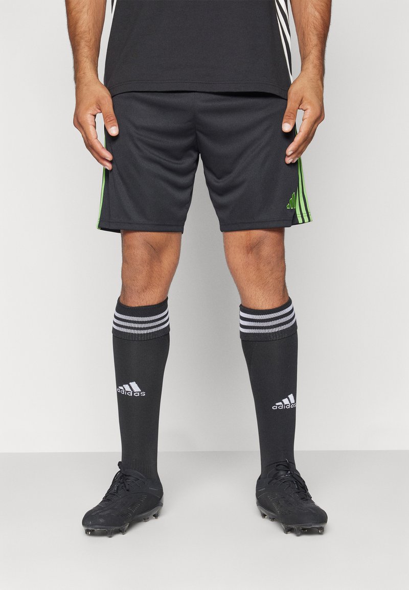Sorte idrettsshorts med grønne striper, kombinert med sorte sokker med hvite striper og hvit logo, samt sorte fotballsko.