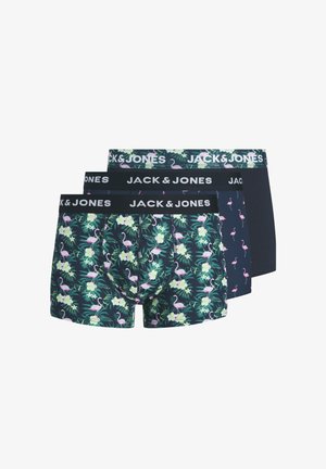 Jeune homme debout, portant un boxer foncé avec un imprimé flamant rose et feuille verte, et une ceinture "JACK & JONES", fond neutre.
