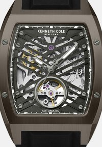 Automatik-Uhr mit einem schwarzen Skelett-Zifferblatt, silberner Hardware und goldenen Akzenten. Verfügt über ein filigranes Design mit sichtbaren Zahnrädern und einem strukturierten Armband.