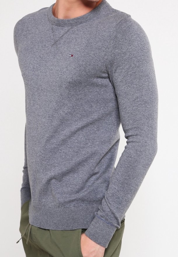 Šedý svetr s dlouhým rukávem vyrobený z měkké látky, s kulatým výstřihem a žebrovanými manžetami. Malý detail s logem na hrudi.