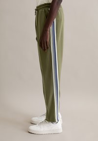 Groene sportbroek met zijstrepen in wit en marineblauw. Voorzien van een trekkoord in de tailleband en een taps toelopend model. Gecombineerd met witte sneakers.