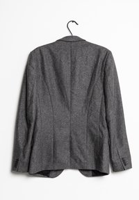 Grå herringbone-blazer med en strukturerad design, spetsiga revär, och en enda slits bak. Har knappelement vid ärmarna.