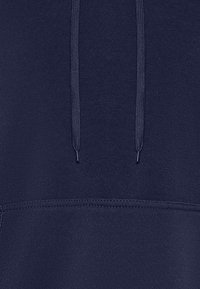 La sudadera azul marino presenta una tela texturizada, cordones con extremos metálicos y un bolsillo tipo canguro. Costura limpia a lo largo del dobladillo.