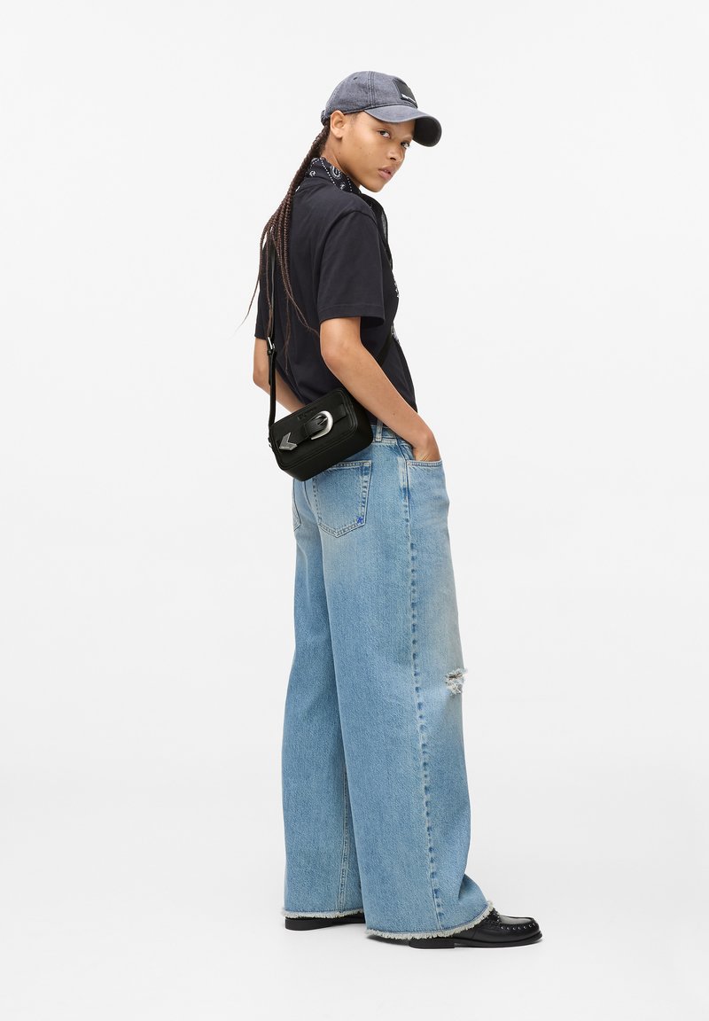 Černé tričko, světle modré široké džíny s děravým detailem, šedá čepice, černá crossbody taška se stříbrným kováním, černé boty.