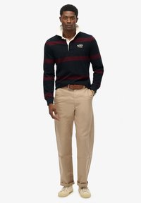 Marineblå og vinrød stribet rugbytrøje med hvid krave, parret med beige bukser og lysfarvede sneakers. Lange ærmer og afslappet pasform.