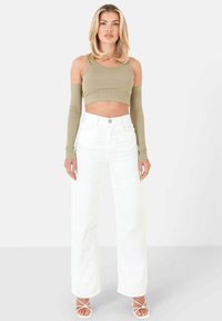Olivgrön croppad tanktopp med långa ärmar, som kombineras med höga vita byxor med vida ben. Har knäppning fram och framfickor.