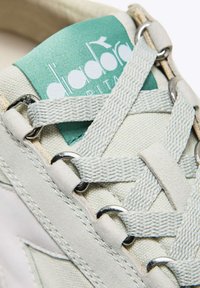 Sneaker bianca in tela con etichetta verde menta, occhielli argentati e lacci testurizzati. Presenta dettagli cuciti e un design a punta rotonda.