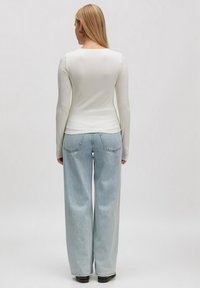Weißes Langarmhemd aus geripptem Stoff, kombiniert mit hellblauen High-Waist-Jeans mit weitem Bein, von hinten betrachtet vor einem schlichten Hintergrund.