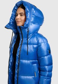 Glänsande blå vadderad jacka med en stor vadderad huva, svart dragkedja och justerbara dragskor. Sidficka med synlig varumärkesetikett.