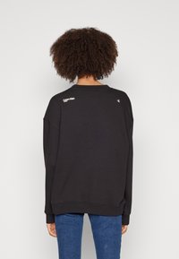 Černá volná mikina s žebrovaným kulatým výstřihem, s bílým logem Calvin Klein na zádech. Texturovaná látka, volný střih.