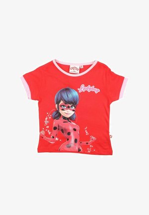 T-shirt en coton rouge à manches courtes, présentant un graphisme de personnage avec des taches noires et des cheveux bleus, le texte "Coccinelle" et des finitions roses.