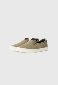 Beige slip-on cipők, texturált anyagból készült, fekete akcentussal a bokánál és fehér gumitalppal.