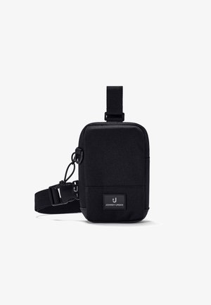 Compacte zwarte crossbodytas met verstelbare riem en een vooraan geplaatste patch met de tekst "Johnny Urban" tegen een witte achtergrond.