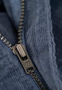 Navy blue fabric with a textured surface, featuring a black metal zipper and YKK branding. Close-up view emphasizing the zipper detail.