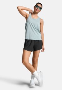 Top sportivo senza maniche azzurro chiaro e pantaloni corti neri. L'outfit ha una vestibilità comoda ed è abbinato a scarpe sportive bianche e calze.