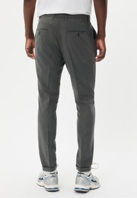 Grå dressbyxor med en elegant design, slim fit, bakfickor med knappar och en slät yta. Bärs med träningsskor.