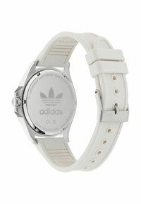 Baltas silikono dirželio laikrodis su nerūdijančio plieno korpusu, apvalios formos, su įspaustu atvirkščiu paviršiumi ir sidabrinėmis detalėmis. Dirželyje yra Adidas logotipas.