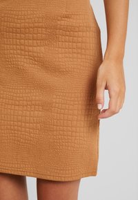 Hnědá texturovaná sukně s mřížkovaným vzorem, vyrobená z měkkého materiálu. Má rovný střih a lem končící nad kolenem.