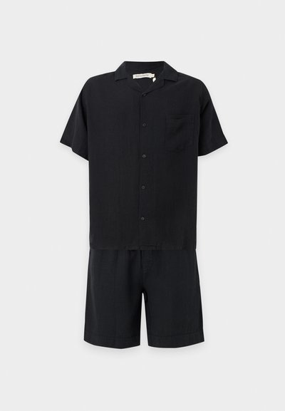 Chemise noire à manches courtes avec boutons et poche poitrine, associée à un short noir assorti sur fond blanc.