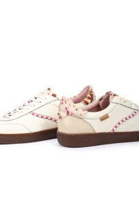 Zapatillas de piel blanca con costuras rosas, acentos texturizados en beige y detalles de piel de vaca en el talón. Suela de goma marrón. Diseño casual.