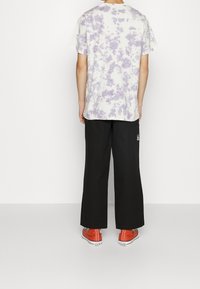 T-shirt i tie-dye i vitt och lavendel, kombinerad med svarta vida byxor och orangea sneakers, sedd bakifrån.