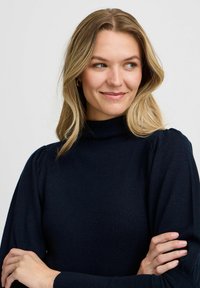 Mörkblå tröja med hög krage, ribbat mönster och puffärmar. Tillverkad av mjukt tyg med åtsittande muddar och en ren design.