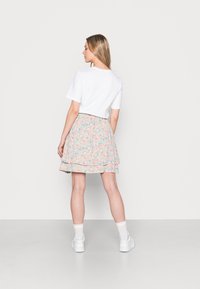 T-shirt cropped branco combinado com uma saia floral em tons suaves de rosa, azul e creme; design em camadas; e ténis brancos.