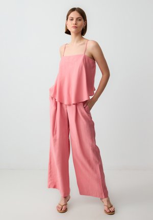 Losse, roze, mouwloze top met een uitlopende snit en een paar bijpassende wijde broek. Zacht materiaal, minimalistische stijl, zijzakken.