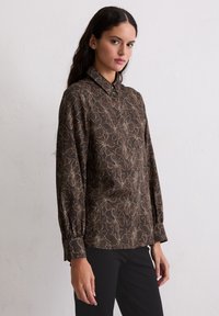 Brązowa koszula na guziki z kwiatowym wzorem w beżu i jasnym niebieskim, z długimi rękawami i klasycznym kołnierzykiem. Gładka tekstura materiału.