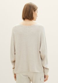 Lichtbeige gebreide trui met ribbelstructuur, brede bootnek en verlaagde schouders. Heeft een naad aan de achterkant en smalle manchetten.