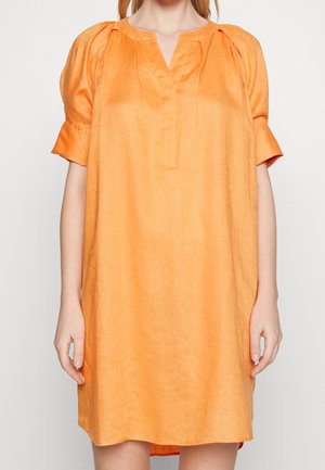 Femme portant une robe ample en lin orange avec des manches mi-ballon et une petite fente en V au col.