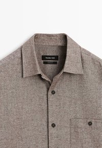 Brun, struktureret skjorte med knaplukning og krave, en brystlomme og sorte knapper. Mærket "Massimo Dutti" synligt indeni kraven.
