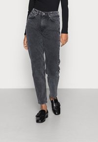 Jeans a vita alta, dritti in denim nero sbiadito con una finitura leggermente strappata. Abbinati a scarpe nere senza lacci con una fibbia.
