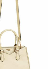 Borsa a mano strutturata beige con due manici superiori e una tracolla rimovibile. Presenta dettagli in oro e una superficie testurizzata. Logo del marchio presente.