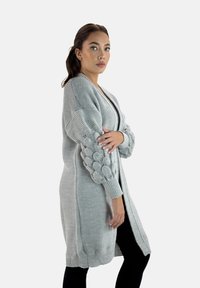 Hellgraue gestrickte Strickjacke mit strukturierten, puffigen Ärmeln, offener Vorderseite und geripptem Saum. Bietet eine lockere Passform und ein mittelkurzes Design.