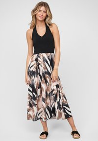 Haut à encolure dégagée noir avec une jupe fluide à motifs présentant des teintes abstraites de marron, crème et noir. Porté avec des sandales à glissière noires.