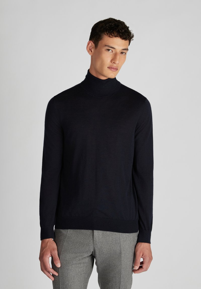 Granatowy sweter z golfem wykonany z delikatnego dzianiny, z długimi rękawami i dopasowanym krojem. Zestawiony z szarymi spodniami o teksturowanej strukturze.