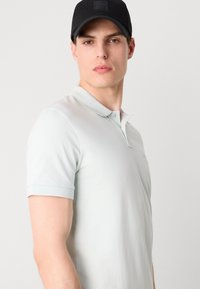 Světle modrá polo košile s krátkými rukávy, měkkou texturou a límečkem. Obsahuje malé logo na hrudi a přiléhavý střih.