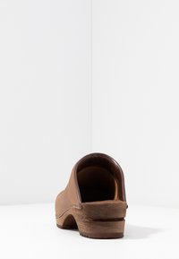 Brown leather clog with a curved design, low heel, and wooden sole. Smooth texture, rounded back, minimal stitching detail.