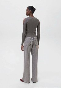 Top grigio a maniche lunghe con dettagli cold-shoulder abbinato a jeans grigi chiari a gamba larga. Texture liscia, design casual, estetica minimalista.