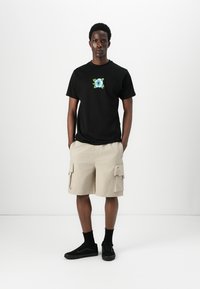 Black cotton t-shirt with floral graphic, cream cargo shorts with four pockets, and black sneakers with a textured surface.