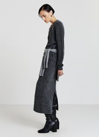 Robe longue en tricot gris foncé avec un col en V, des fentes latérales et une ceinture grise. Associée à des bottes en cuir noir montant jusqu'aux genoux.