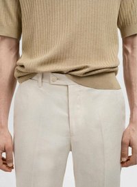 Beige geribbelde gebreide trui gecombineerd met lichtbeige broek met knoopsluiting, wat een casual maar verfijnde uitstraling geeft.