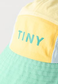Bob patchwork avec des panneaux jaunes, bleu clair et vert menthe, arborant le mot "TINY" en lettres bleu sarcelle sur un patch jaune.