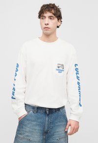 Λευκό μακρυμάνικο T-shirt με μπλε γραφικά, που διαθέτει τσέπη, και άνετο τζιν σορτς με μπροστινές τσέπες.