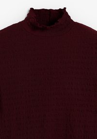 Top burdeos de cuello alto con una tela texturizada, que presenta un cuello con volantes y un corte ligeramente holgado, adecuado para superponer.