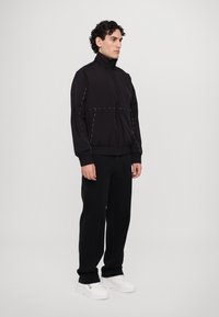 Schwarze leichte Jacke mit hohem Kragen, elastischen Bündchen und kontrastierenden weißen Nähten. Kombiniert mit schwarzen Hosen und weißen Sneakers.