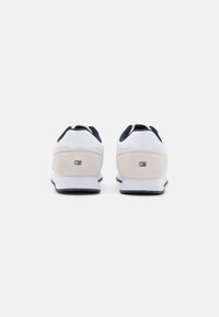 Sneakers bianchi con accento in suede grigio sul tallone, tessuto nero al colletto e suola in gomma testurizzata con dettaglio del logo.